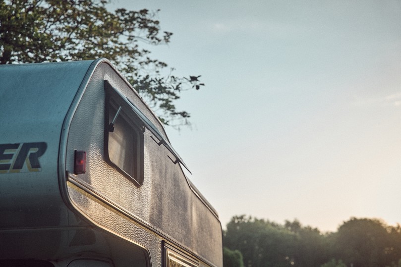 Side of a motorhome in the evening sun, with open window and trees in the background